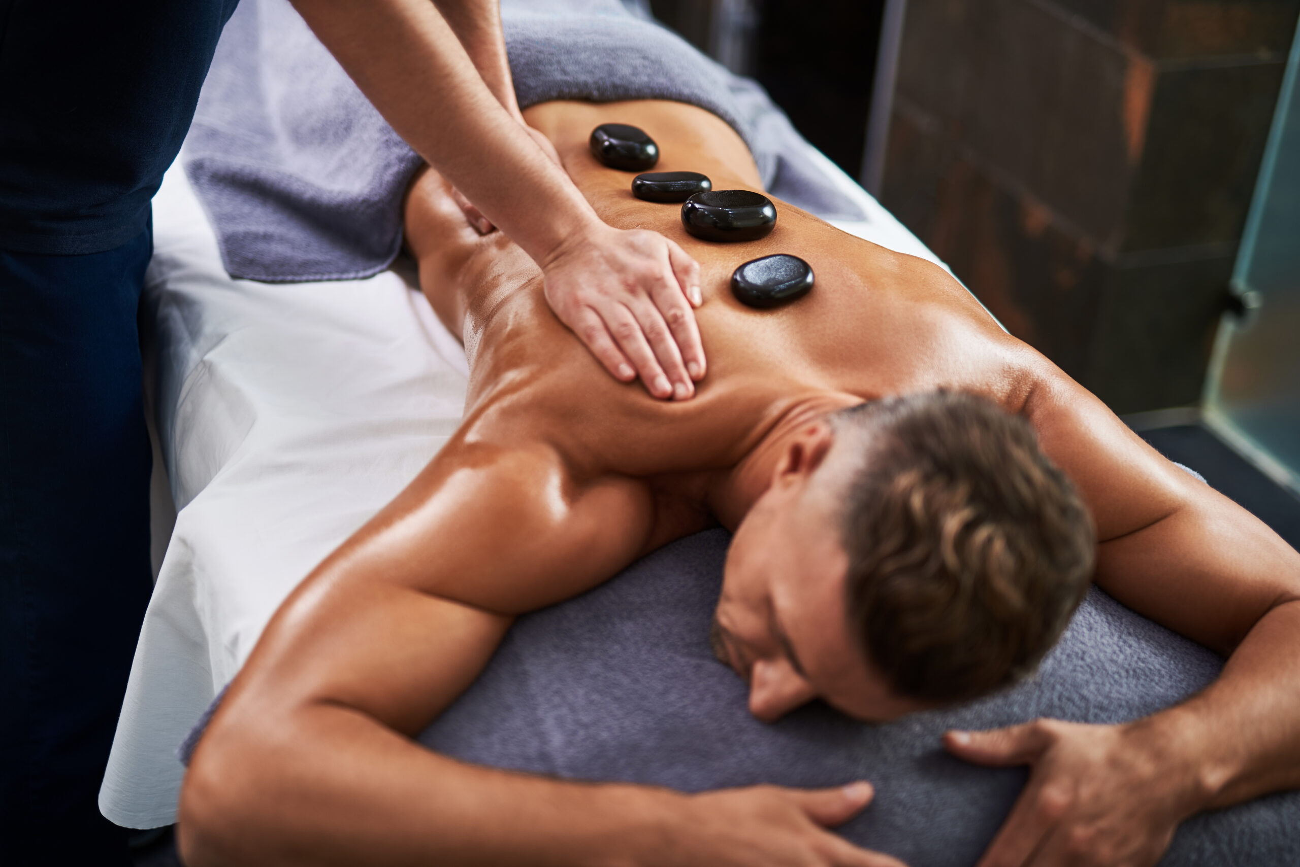 Professional masseur massaging client body while he lying on massage table