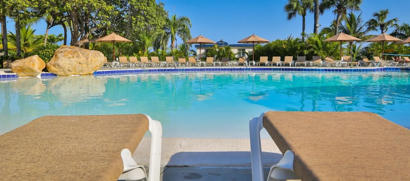 Pool with lounge chairs, umbrellas, rocks, and palms at Lifestyle Tropical Beach Resort & Spa.