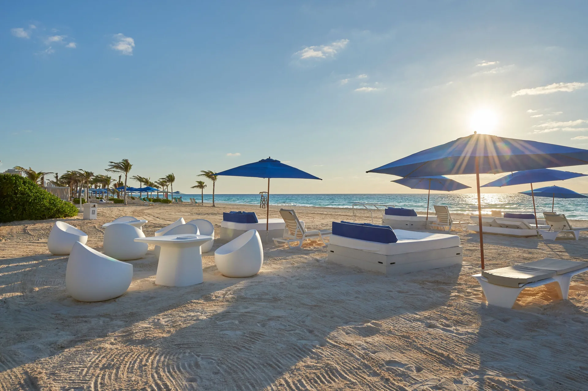 Beach lounge seating and blue umbrellas at sunset at Live Aqua Cancun.