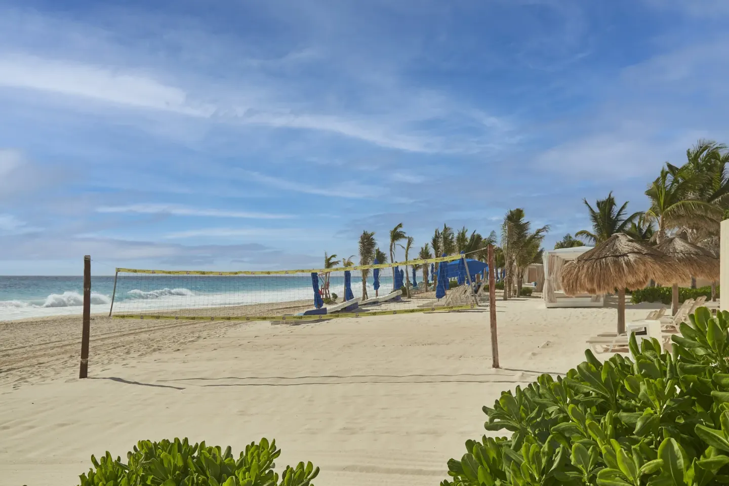 Beach volleyball net, loungers, palms, and ocean waves at Live Aqua Cancun.