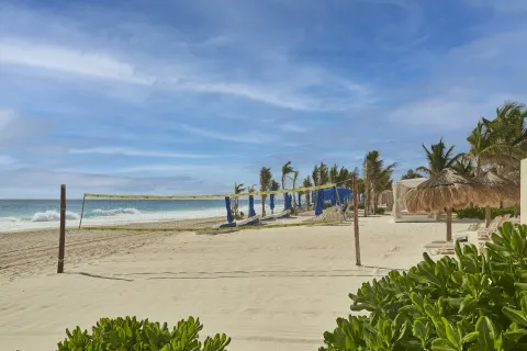 Beach volleyball net, loungers, palms, and ocean waves at Live Aqua Cancun.