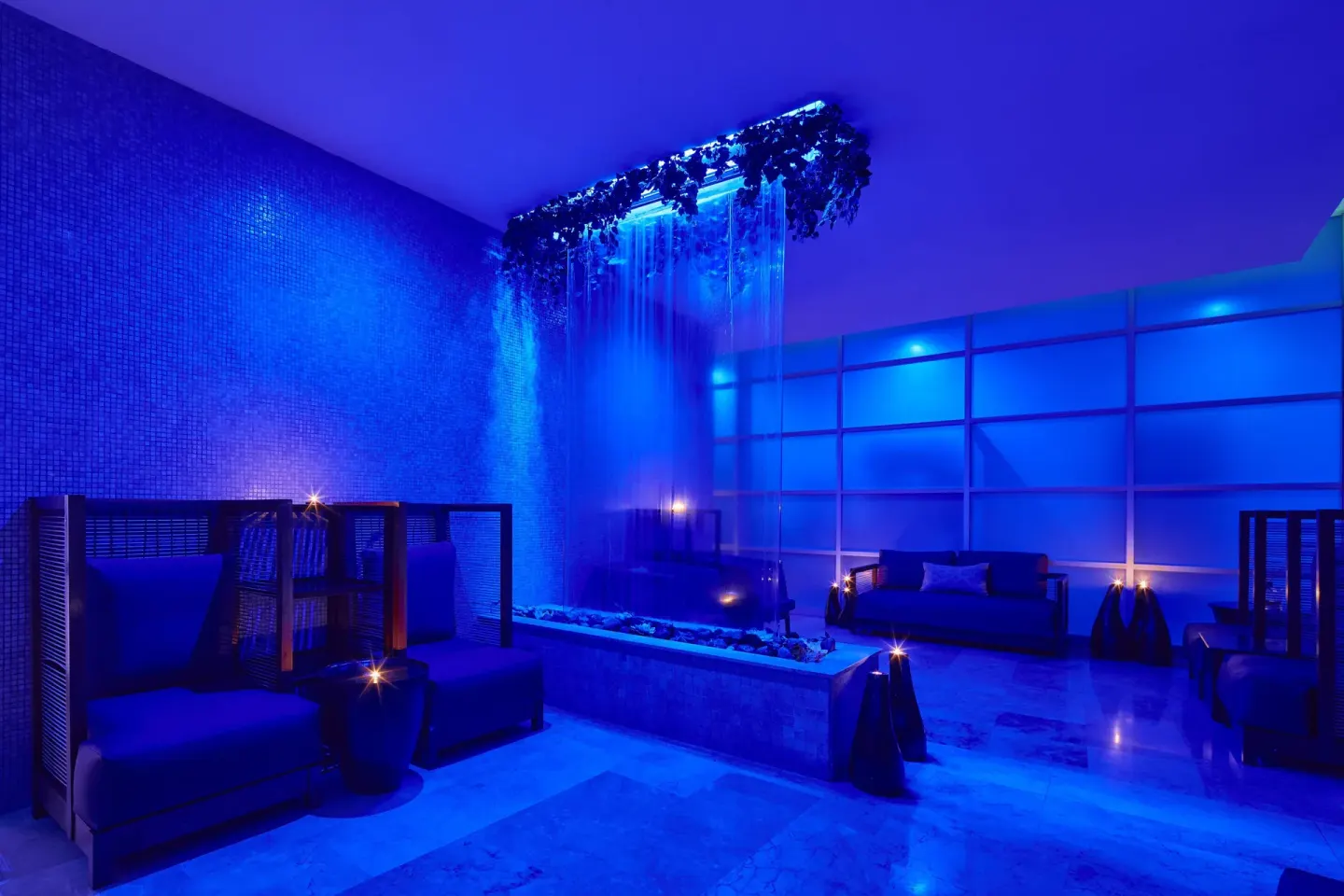 Blue-lit spa lounge with waterfall feature and seating at Live Aqua Cancun.