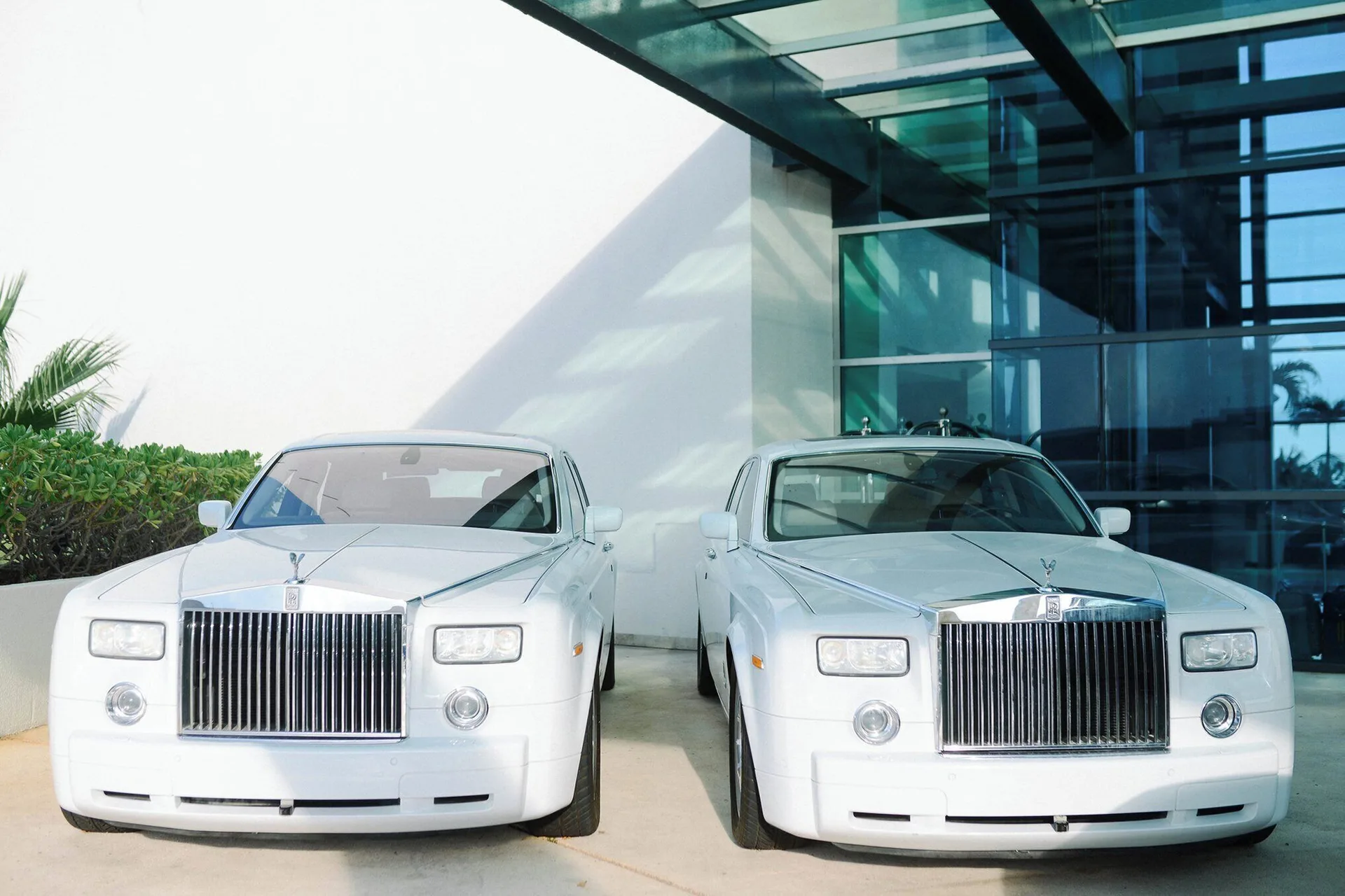 Two white luxury cars parked outside the glass entrance at Live Aqua Cancun.