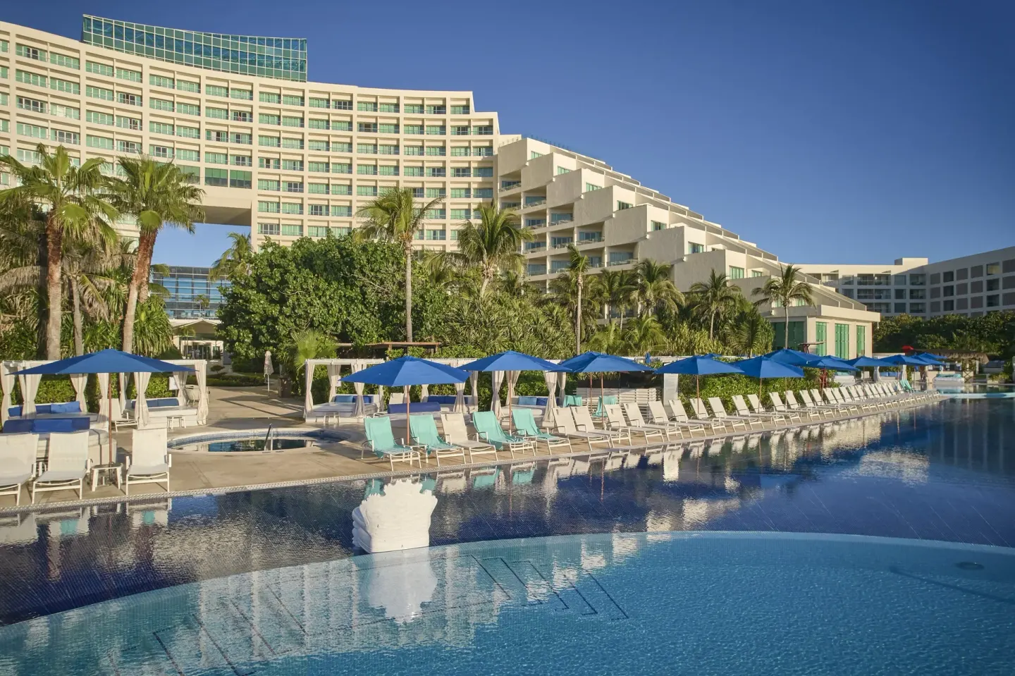 Pool deck with blue umbrellas and resort buildings at Live Aqua Cancun.