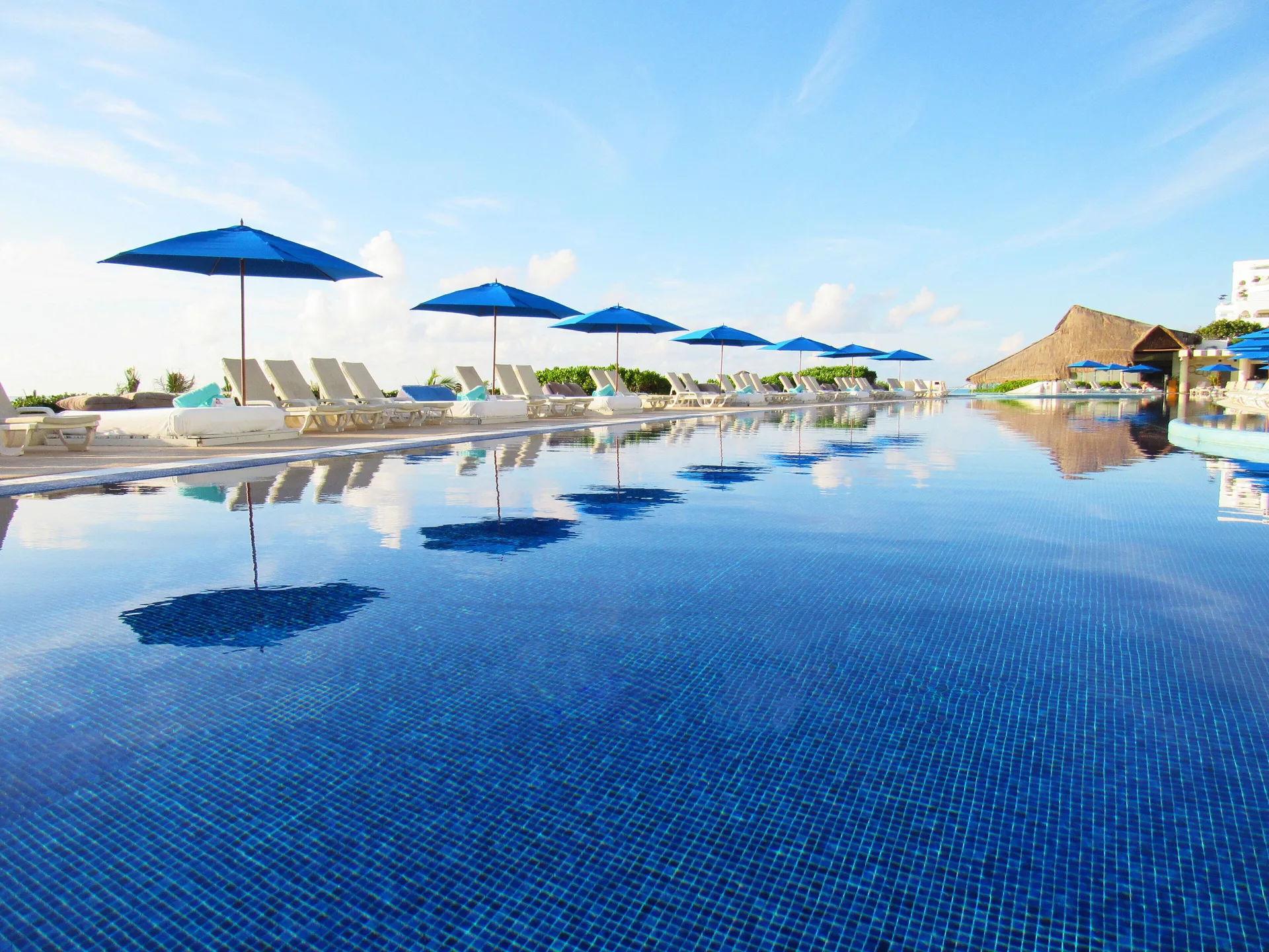 Reflective pool with blue umbrellas and lounge chairs at Live Aqua Cancun.