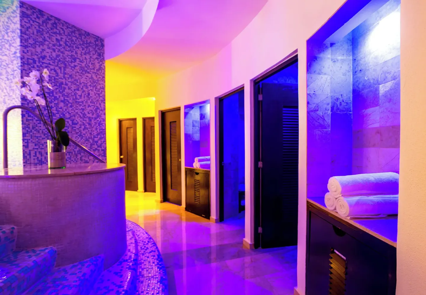 Spa corridor with tiled rooms, rolled towels, and colorful lighting at Live Aqua Cancun.