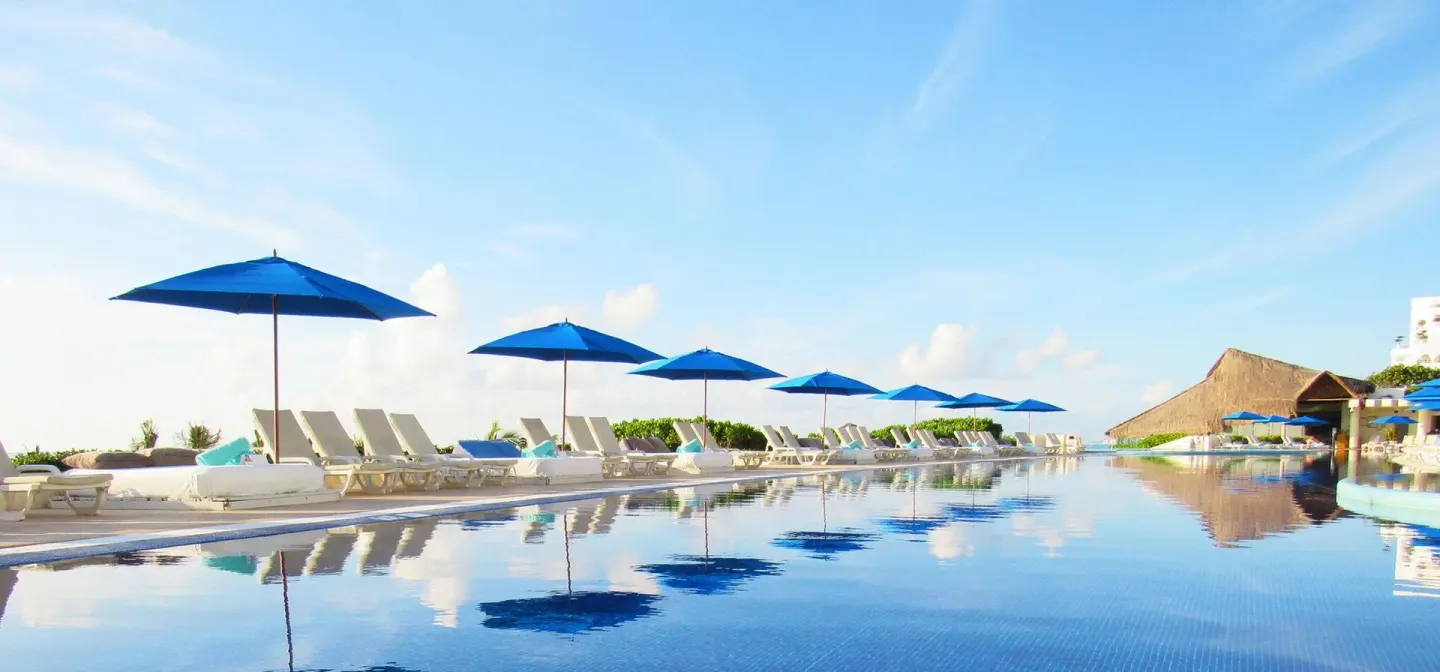 Wide pool view with blue umbrellas and white loungers at Live Aqua Cancun.