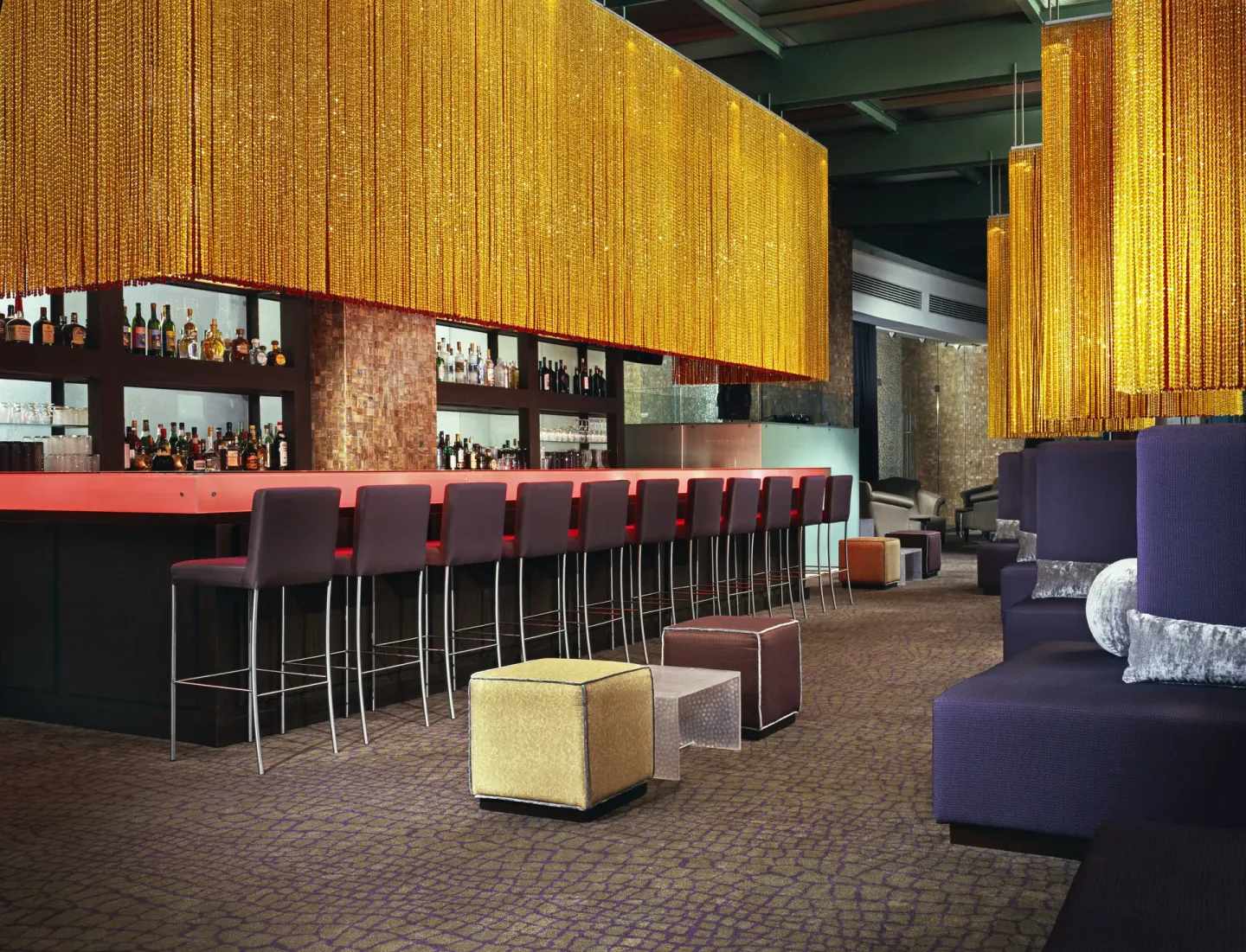 Lounge bar with red counter, stools and gold hanging strands at Live Aqua Cancun.