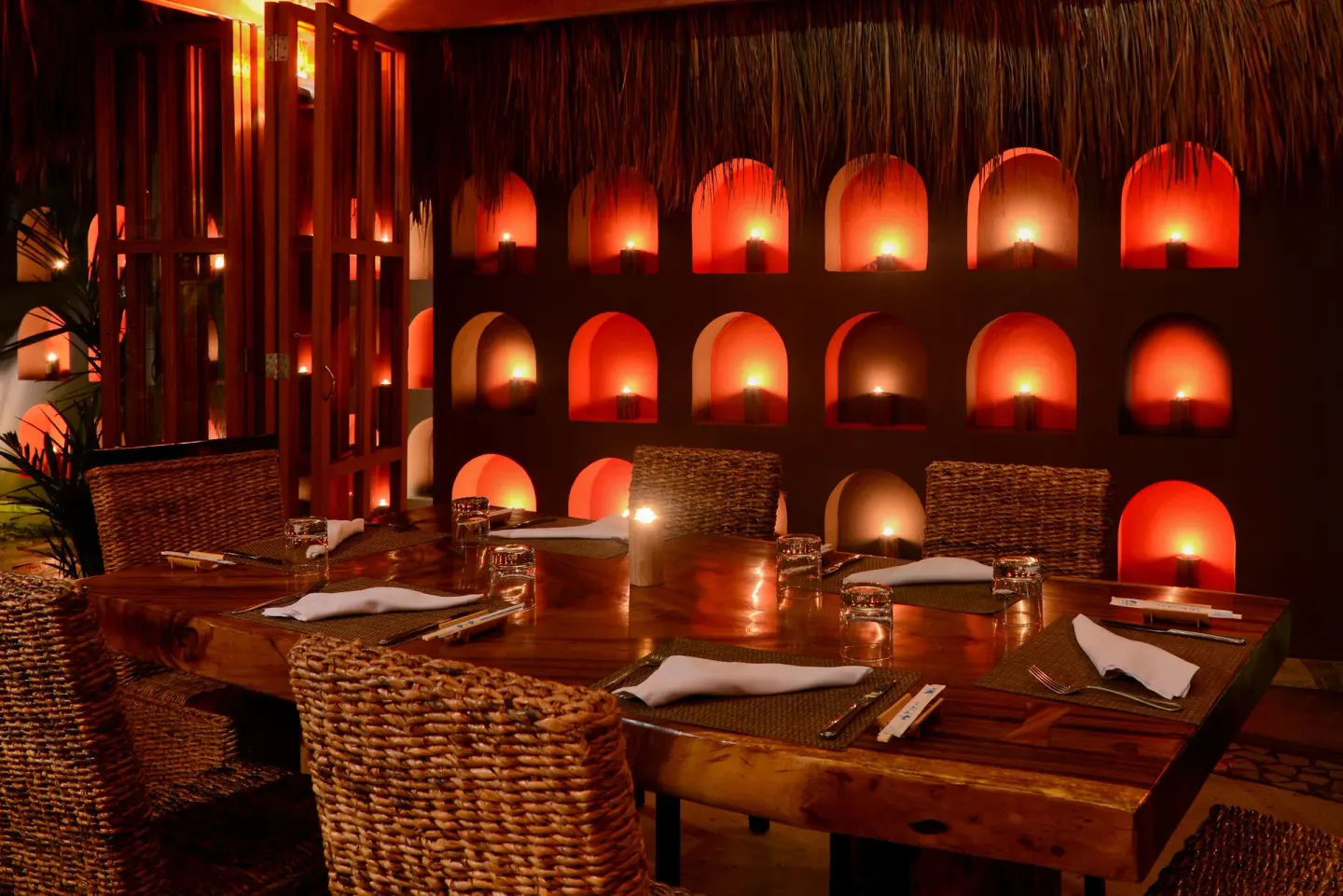 Candlelit dining table with woven chairs inside a thatched room at Live Aqua Cancun.
