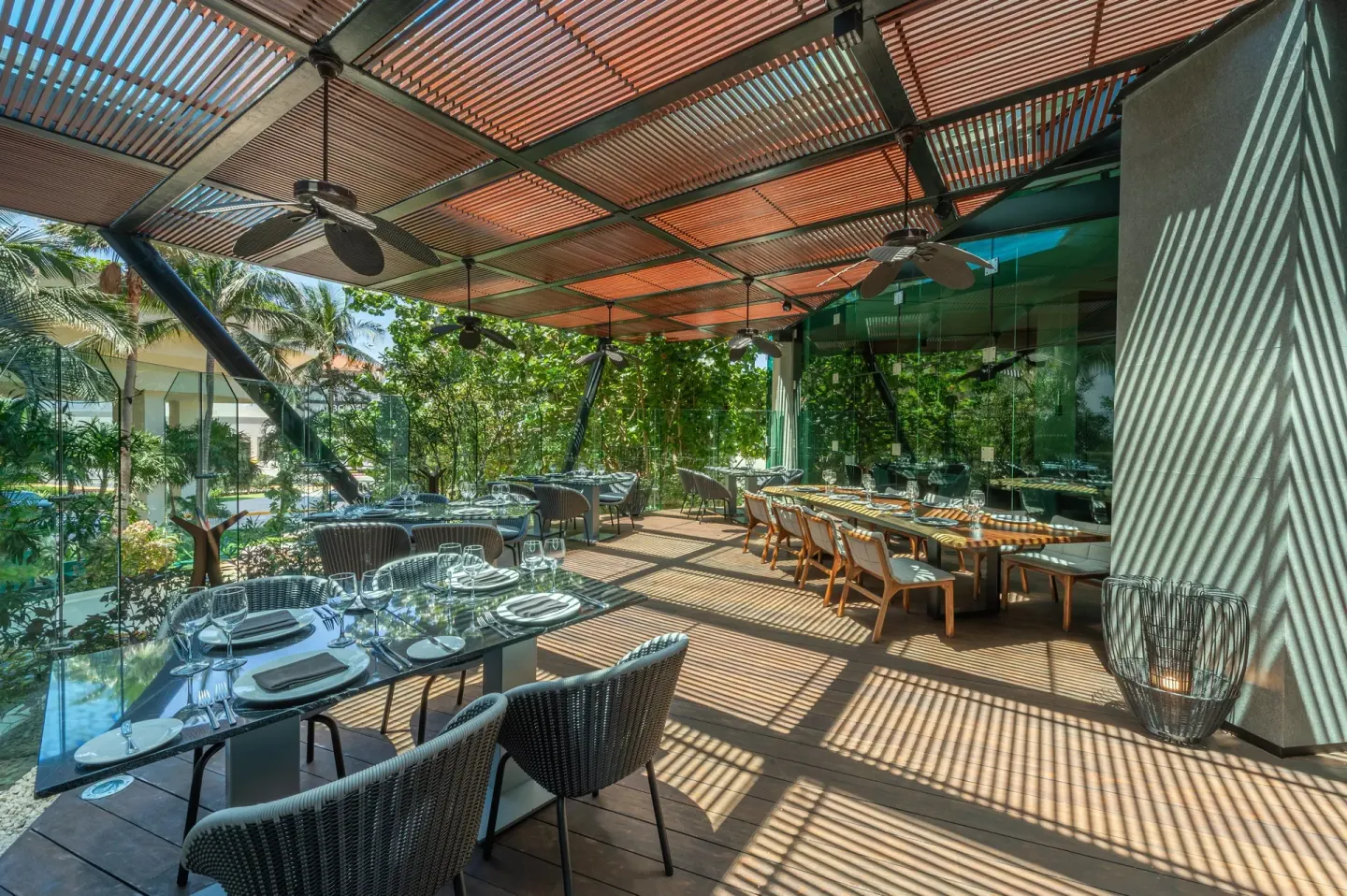 Bright dining terrace with glass tables, greenery, and slatted shade at Live Aqua Cancun.
