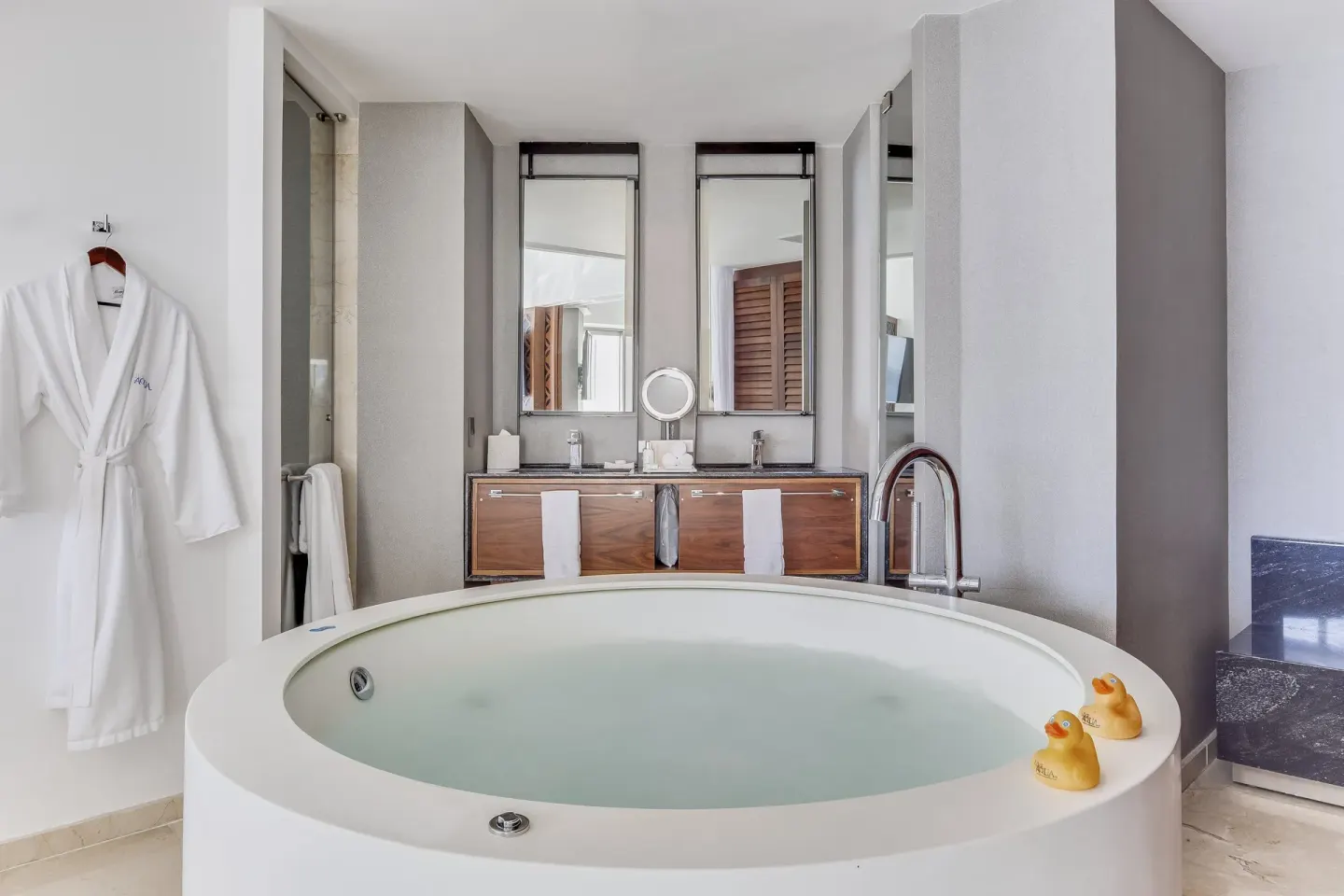 Round jetted tub, double vanity, and robe in an oceanfront suite bathroom at Live Aqua Cancun.