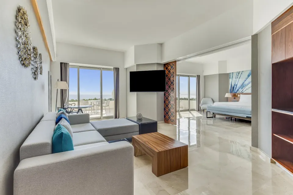 Oceanfront suite living area with sofa, TV, balcony, and bedroom at Live Aqua Cancun.