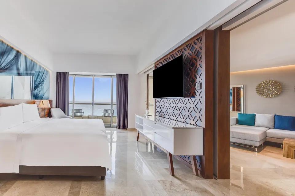 Oceanfront suite bedroom with king bed, TV divider, balcony, and sitting area at Live Aqua Cancun.