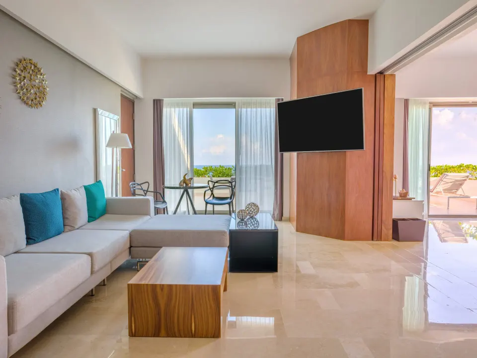 Suite sitting room with sectional sofa, TV, dining table, and ocean-facing windows at Live Aqua Cancun.