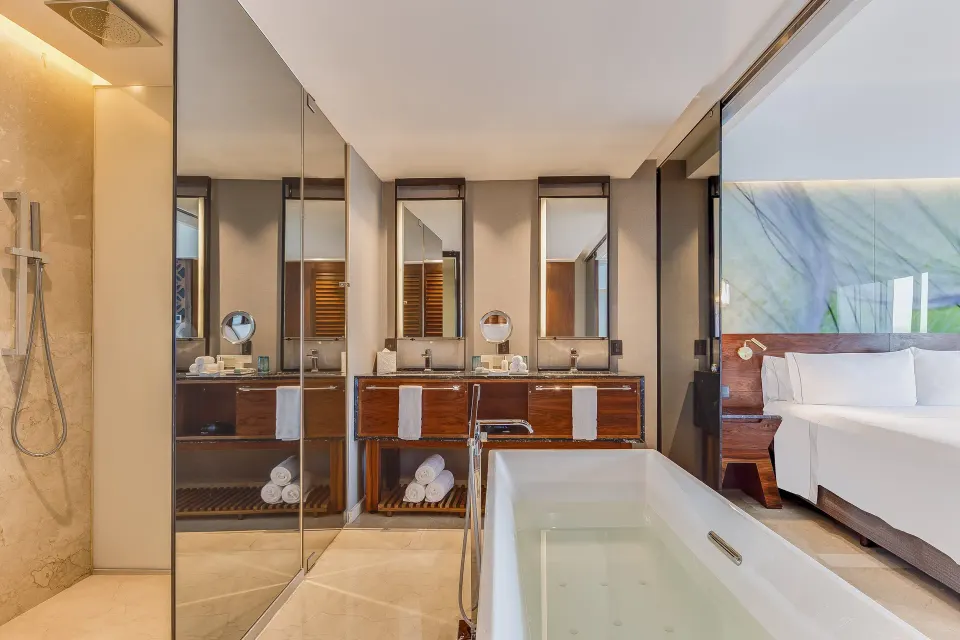 Viento Suite bath area with shower, soaking tub, vanity, and king bed at Live Aqua Cancun.