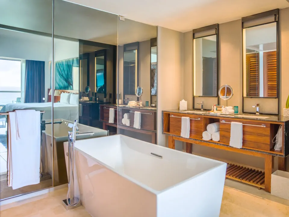 Viento Suite bathroom with tub, mirrored walls, double vanity, and ocean glimpse at Live Aqua Cancun.