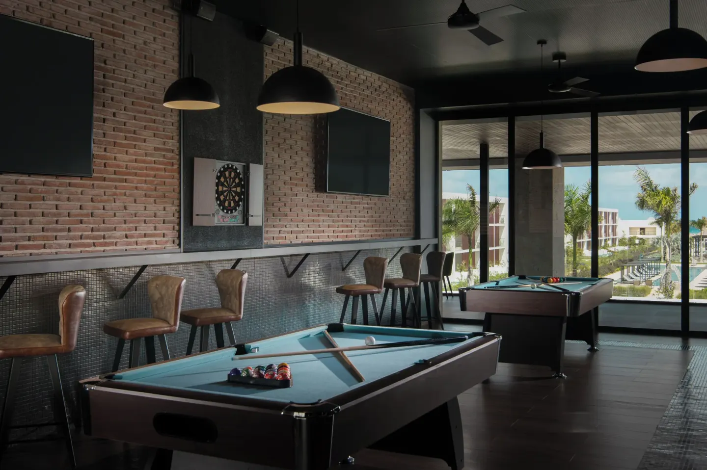 Game room with pool tables, dartboard, bar stools, and large windows at Live Aqua Punta Cana.