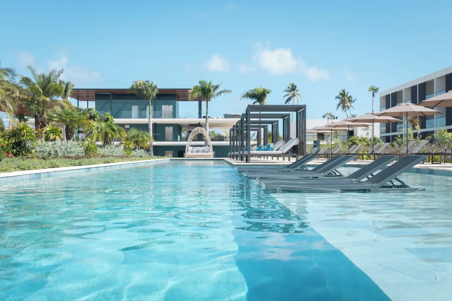 Wide resort pool with in-water loungers, cabanas and palms at Live Aqua Punta Cana.