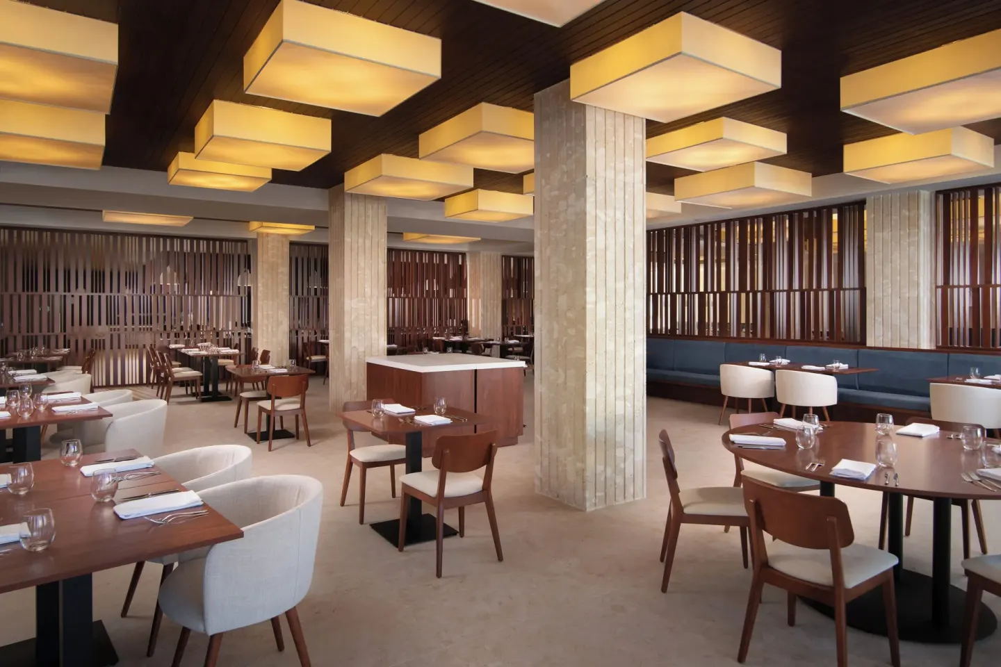 Dining room with square ceiling lights, set tables, and wood screens at Live Aqua Punta Cana.