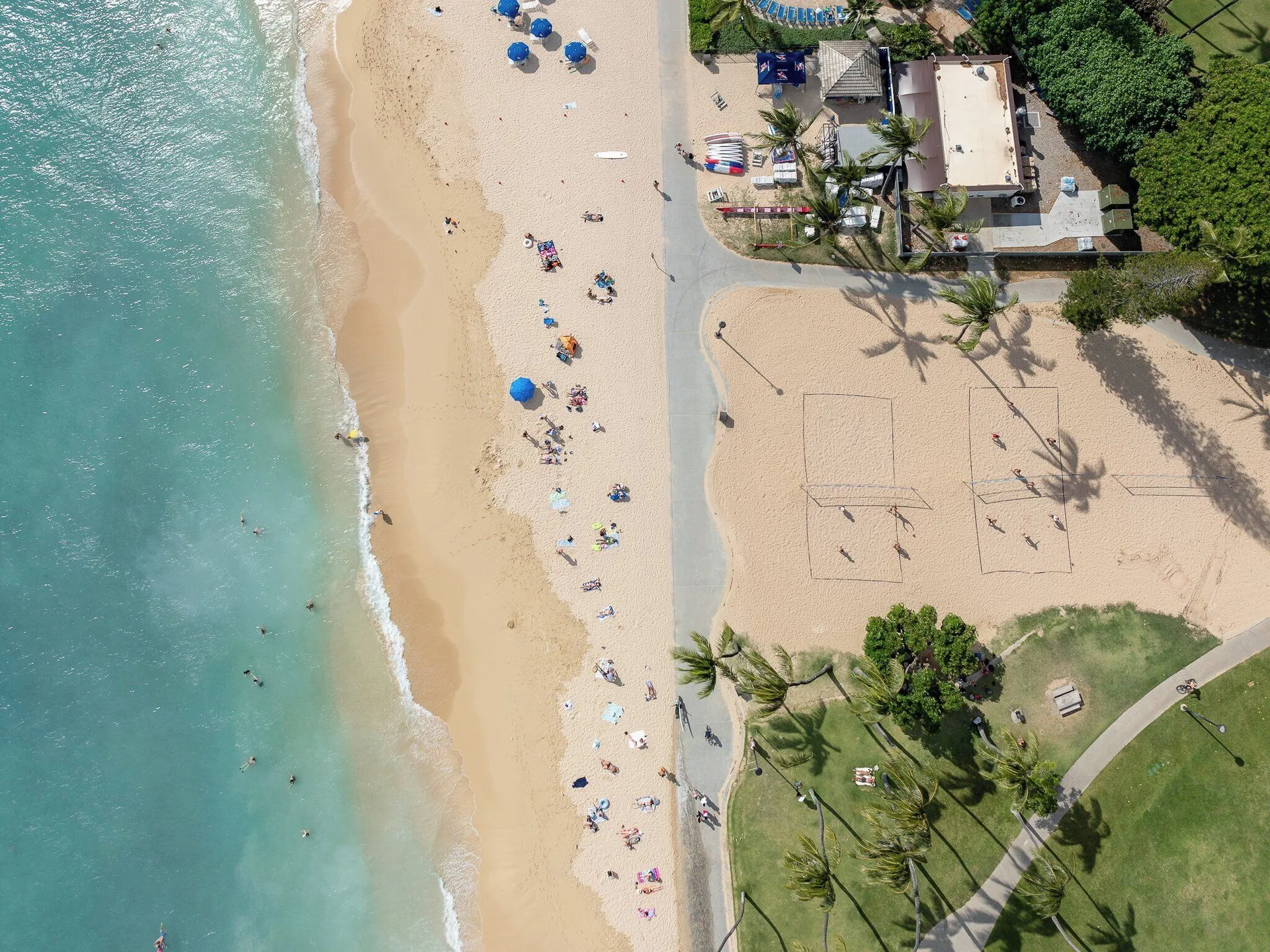 Overhead beach view with swimmers, umbrellas, paths, and sand courts near Luana Waikiki Hotel & Suites.