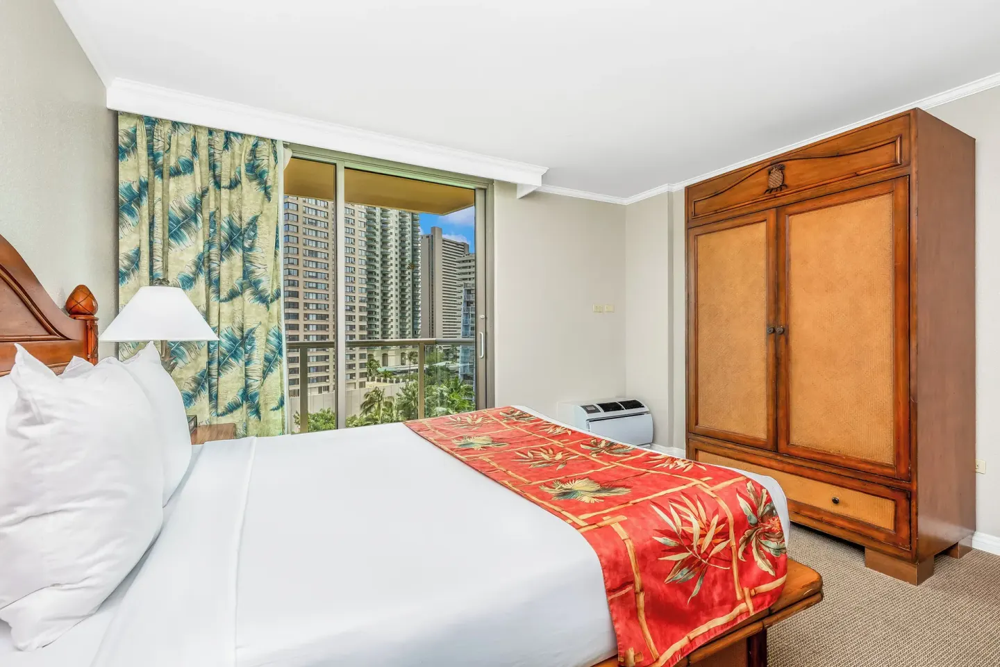 Bedroom with a king bed, wood armoire, and city-view balcony at Luana Waikiki Hotel & Suites.