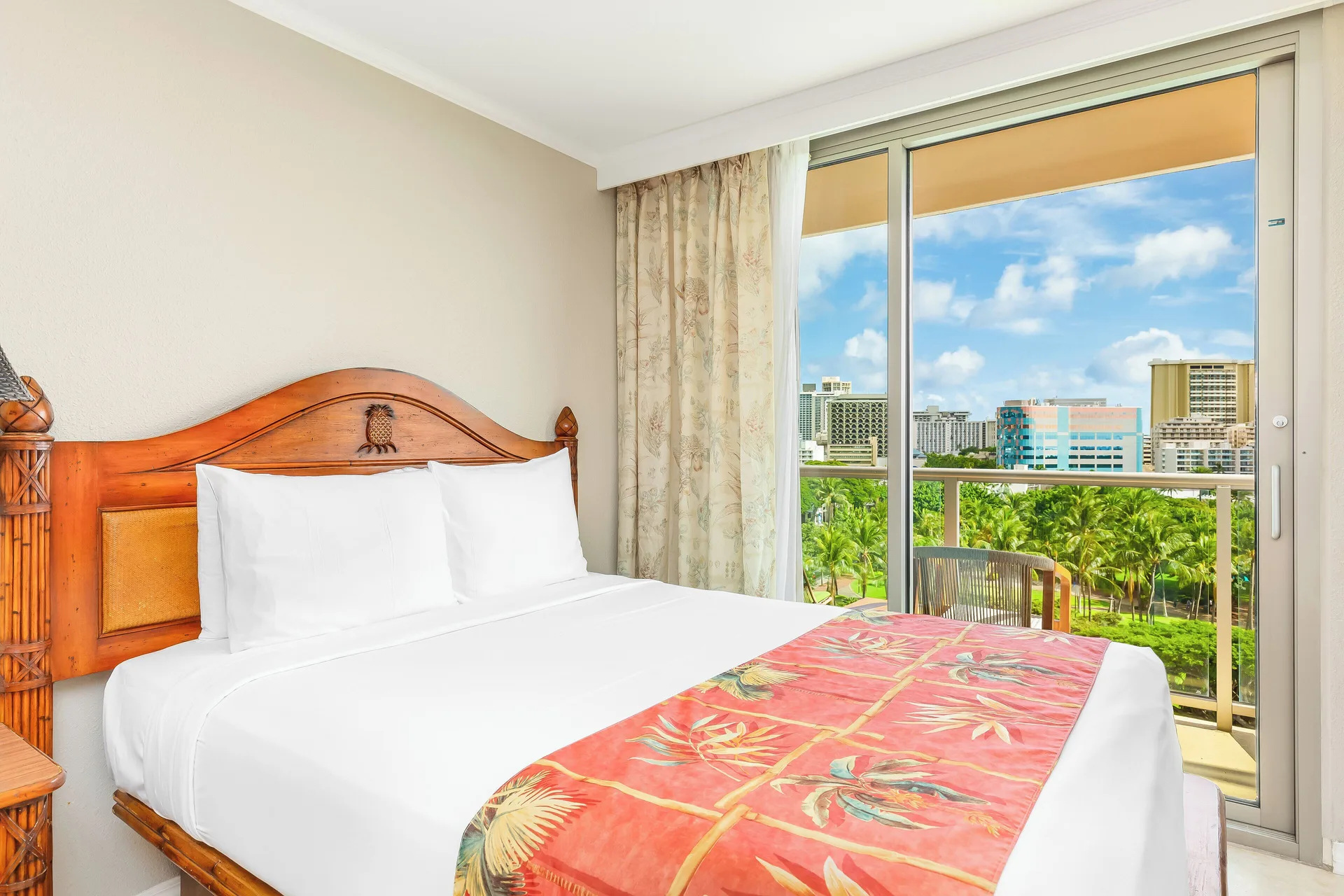 Guest room king bed and balcony city view at Luana Waikiki Hotel & Suites.