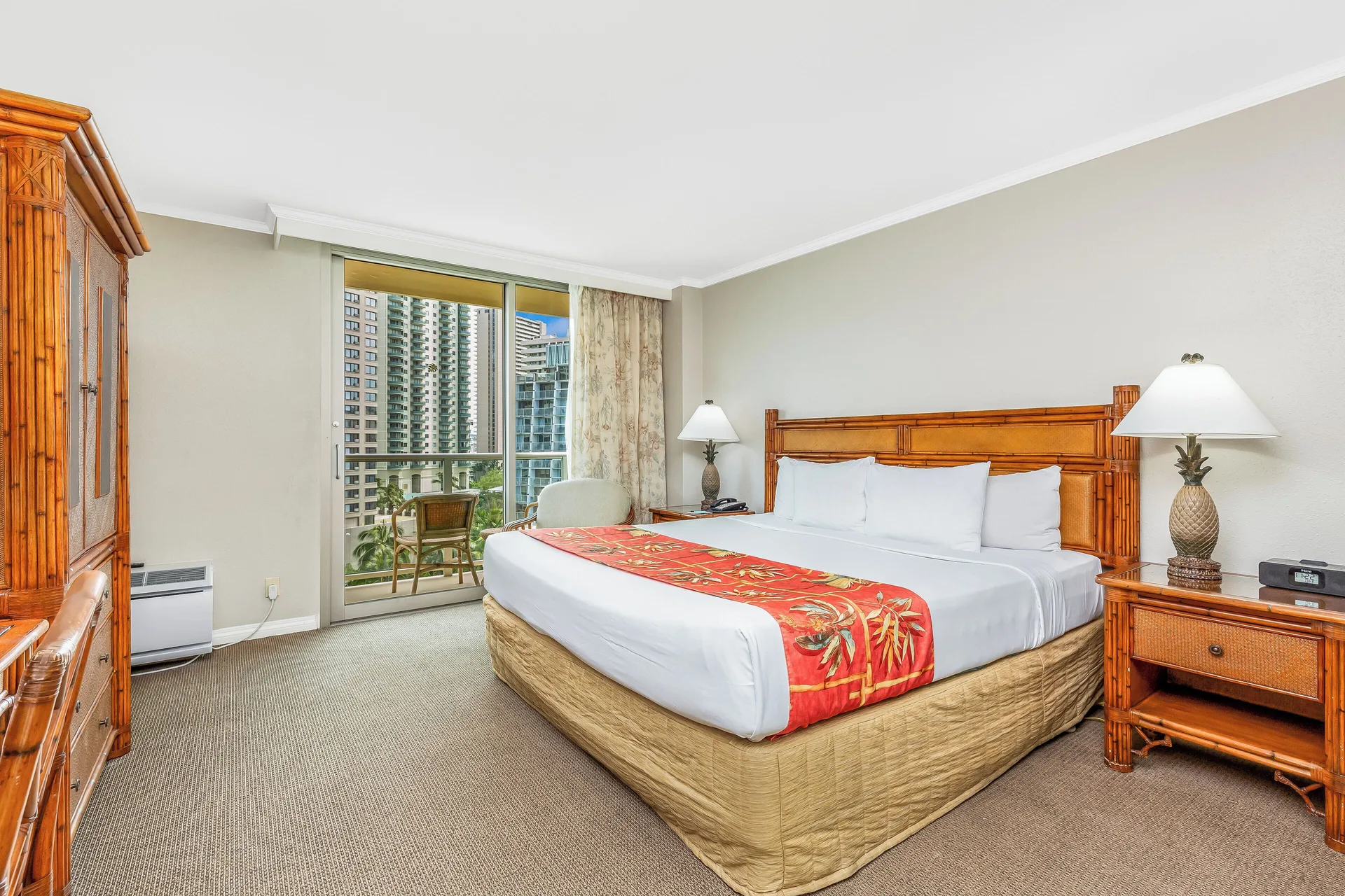 King-bed guest room with balcony and bamboo-style furniture at Luana Waikiki Hotel & Suites.