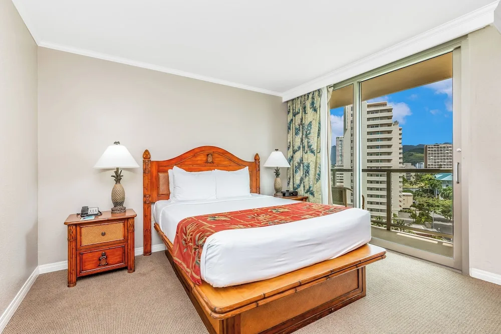 King-bed guest room with city-facing window at Luana Waikiki Hotel & Suites.
