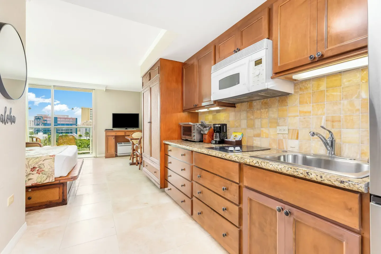 Guest room kitchenette with wood cabinets and a bed beyond at Luana Waikiki Hotel & Suites.