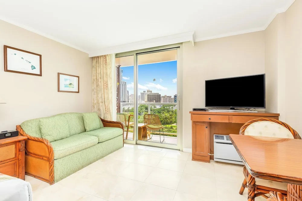 Sitting area with green sofa, TV, dining table, and balcony at Luana Waikiki Hotel & Suites.