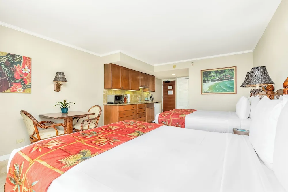 Two beds, a dining table, and kitchenette appear in a guest room at Luana Waikiki Hotel & Suites.