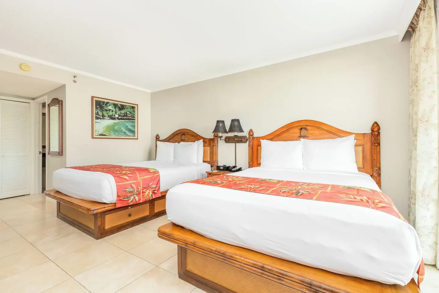 Two beds with tropical runners fill a guest room at Luana Waikiki Hotel & Suites.