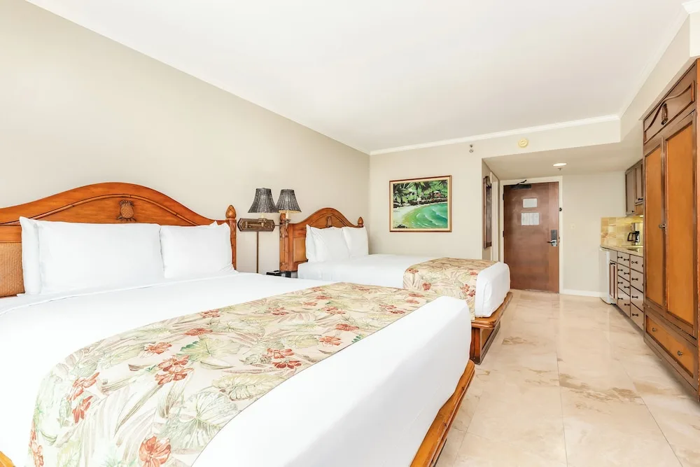 Two beds and wood furnishings are shown in a guest room at Luana Waikiki Hotel & Suites.