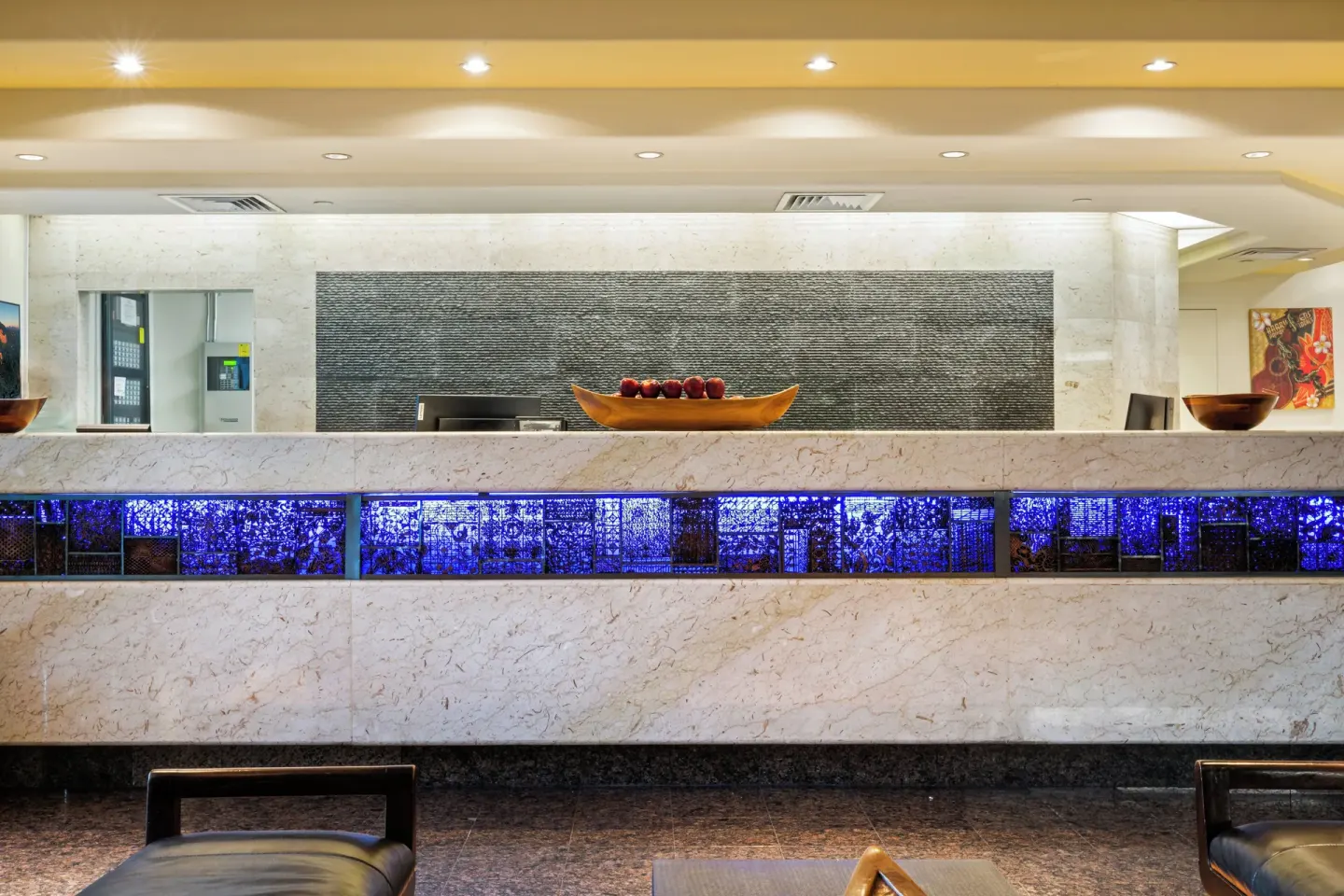 The front desk with blue accent lighting is shown at Luana Waikiki Hotel & Suites.
