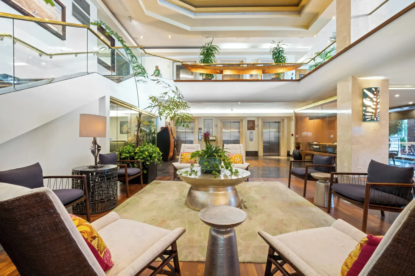 Lobby lounge at Luana Waikiki Hotel & Suites with chairs, planter table, elevators, and mezzanine.