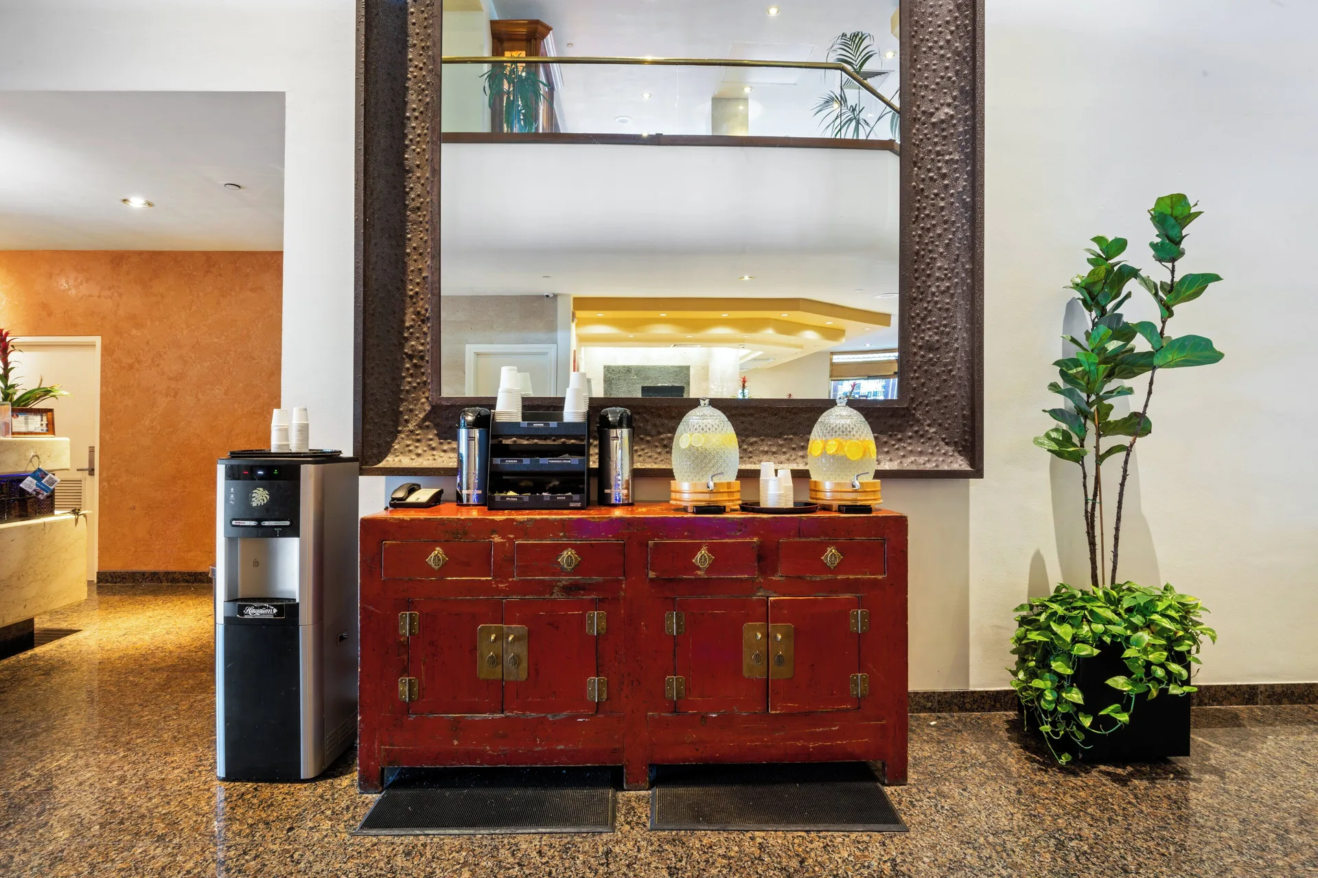 Refreshment station in the lobby at Luana Waikiki Hotel & Suites with infused drinks and plants.
