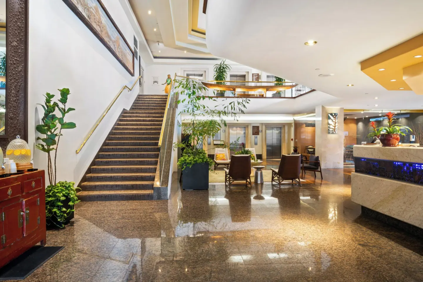 Lobby at Luana Waikiki Hotel & Suites with staircase, reception desk, seating, and plants.
