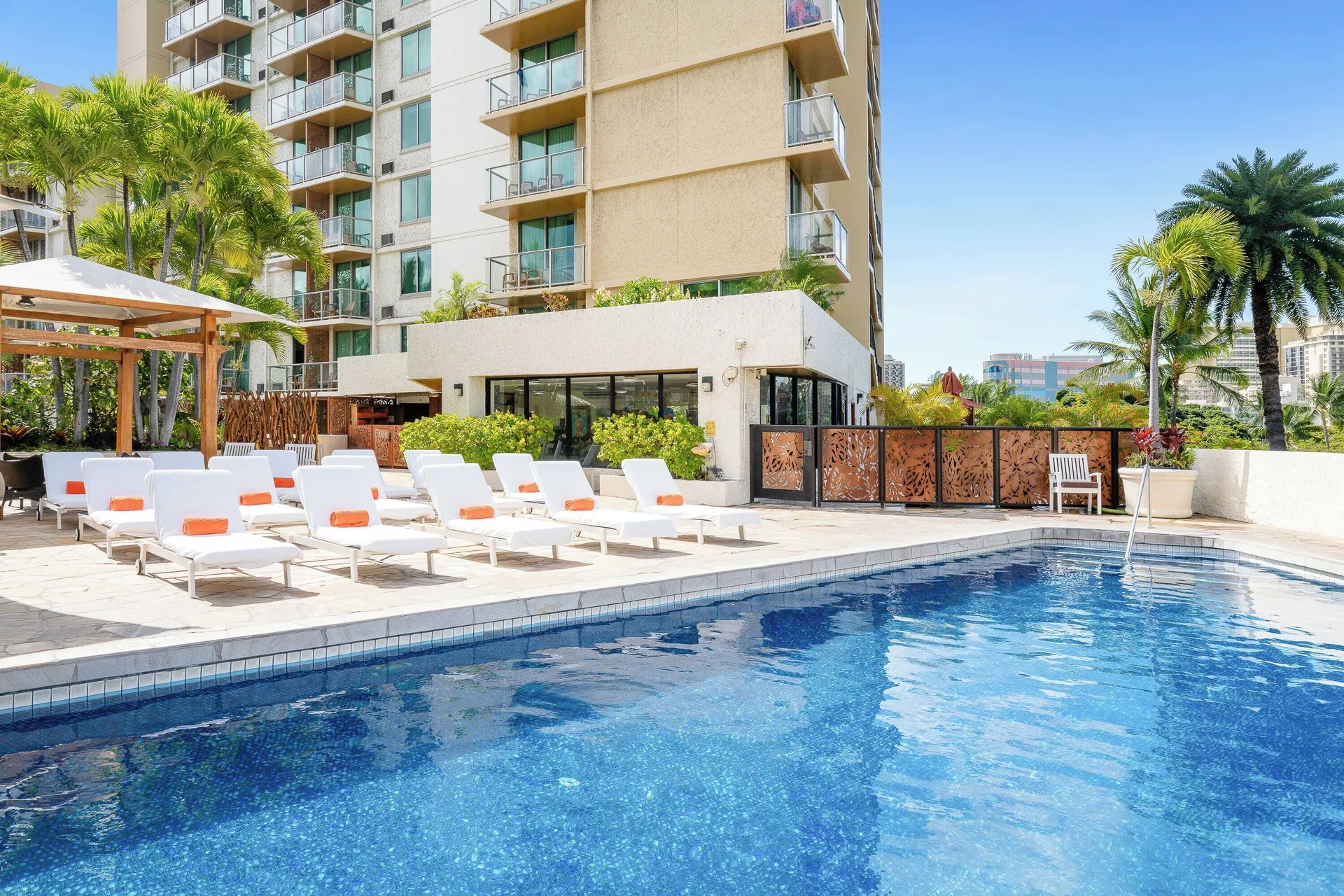 Pool water, lounge chairs, palms, and the hotel tower at Luana Waikiki Hotel & Suites.