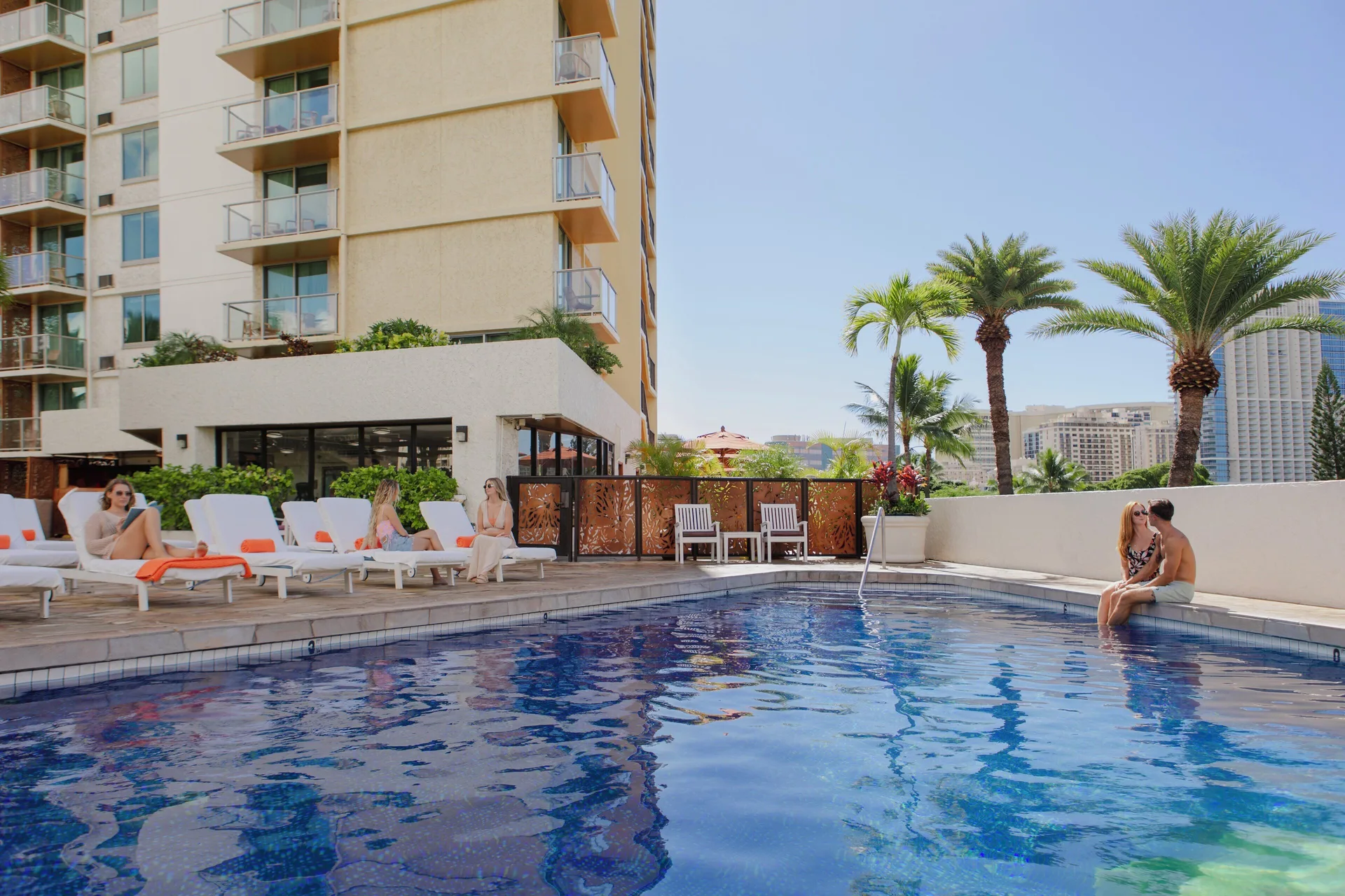Guests relaxing by the pool at Luana Waikiki Hotel & Suites with palms and balconies nearby.
