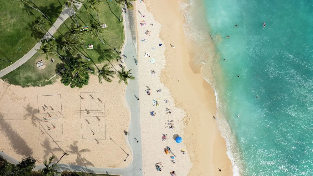 Top-down view of sand courts, beachgoers, and turquoise water near Luana Waikiki Hotel & Suites.