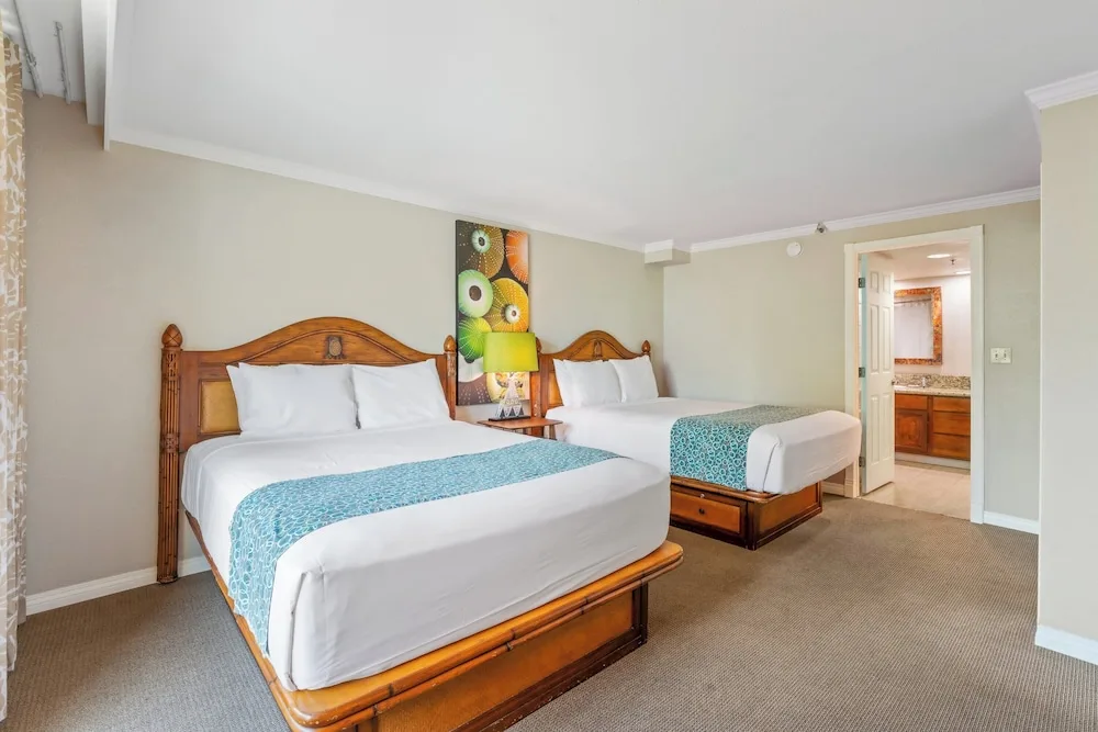 Guest room with two beds, wood headboards, and an open bathroom at Luana Waikiki Hotel & Suites.