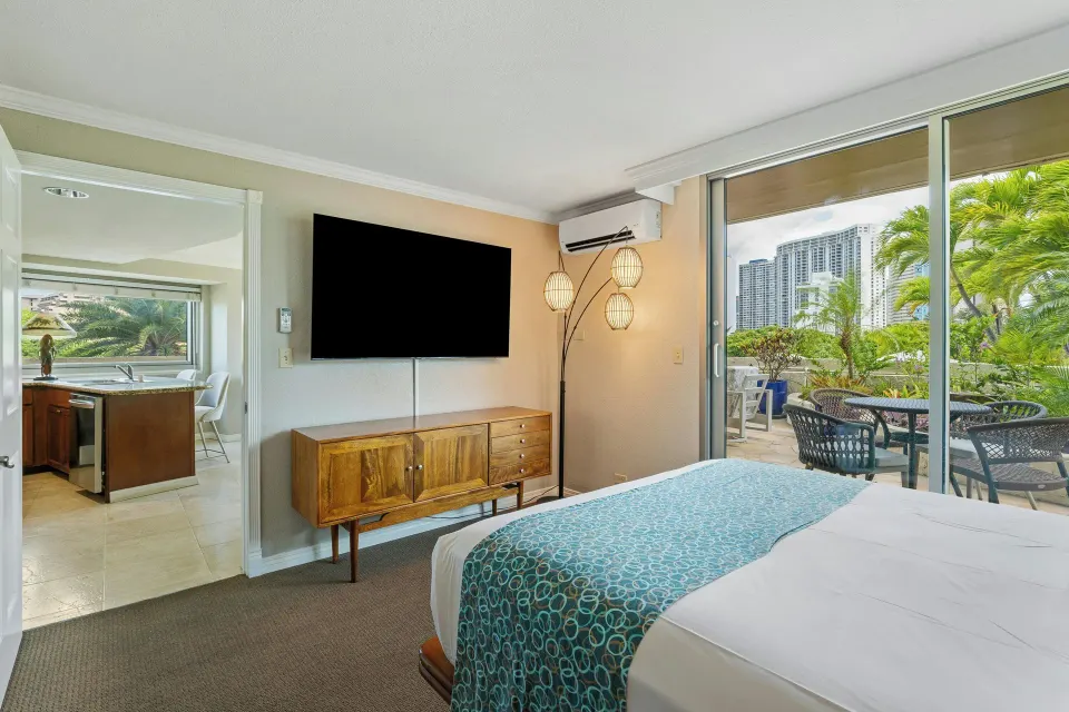 Family suite bedroom at Luana Waikiki Hotel & Suites with bed, TV, kitchen doorway and patio.