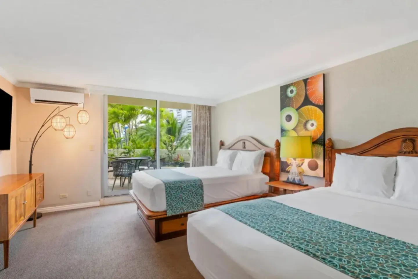 Family suite bedroom at Luana Waikiki Hotel & Suites with two beds and patio doors facing greenery.