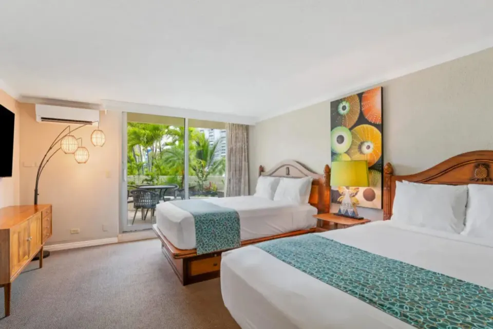 Family suite bedroom at Luana Waikiki Hotel & Suites with two beds and patio doors facing greenery.