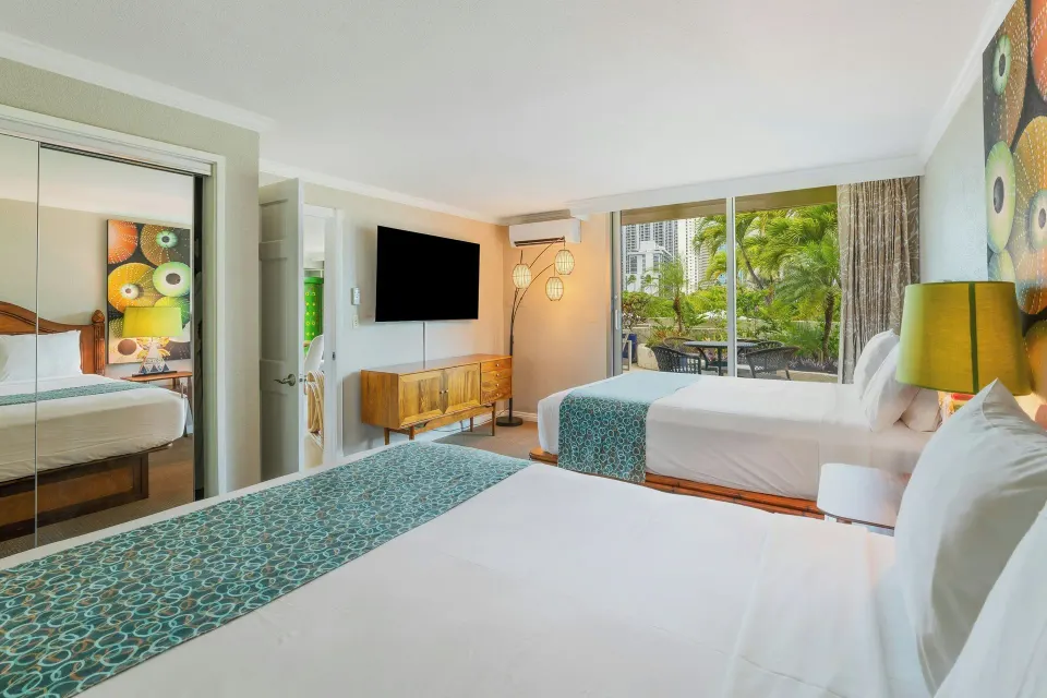 Family suite bedroom at Luana Waikiki Hotel & Suites with two beds, TV and patio view.