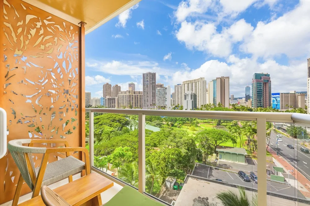 Balcony seating overlooks Waikiki towers and park greenery at Luana Waikiki Hotel & Suites.