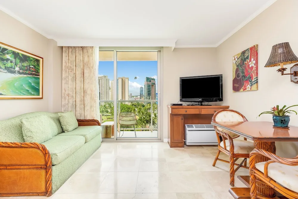 Sofa bed, dining table, TV, and balcony city view in a room at Luana Waikiki Hotel & Suites.