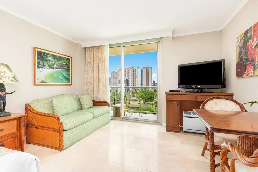 Sofa, balcony doors, TV, and dining table in a city view room at Luana Waikiki Hotel & Suites.