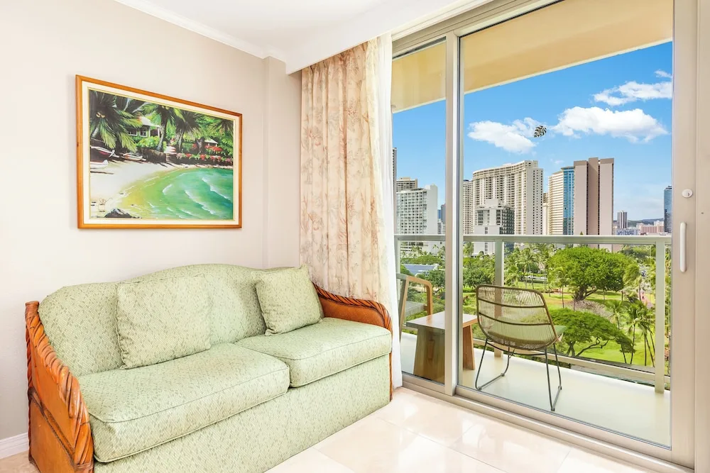 Green sofa beside balcony doors with city views at Luana Waikiki Hotel & Suites.