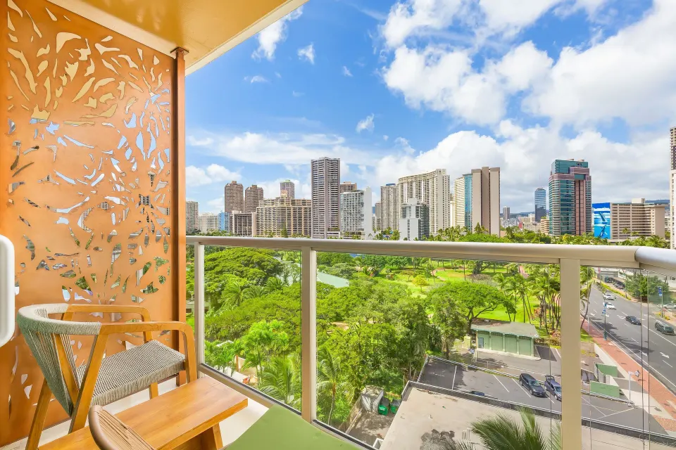 City-view balcony with chair at Luana Waikiki Hotel & Suites overlooking Honolulu skyline and park greenery.